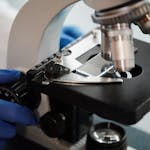 Close-up image of a scientist's gloved hand adjusting a microscope in a research lab.