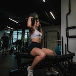 Woman wearing sports bra and shorts exercises on gym bench, promoting fitness and well-being.