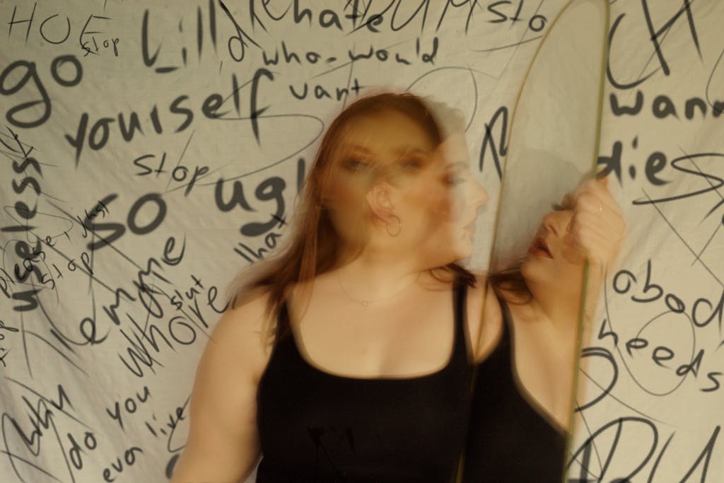 A woman looking at her reflection surrounded by negative words in a blurred image.