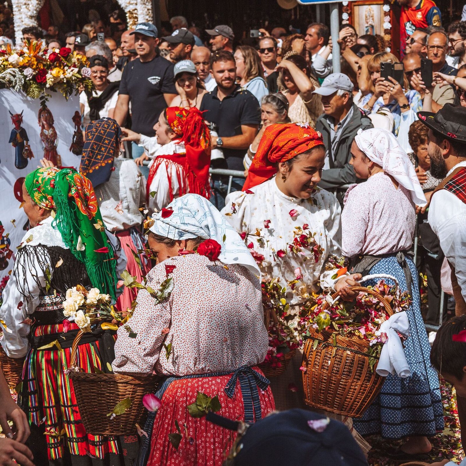 Festive street scene with people in traditional Portuguese attire and flower petals scattered on the street.